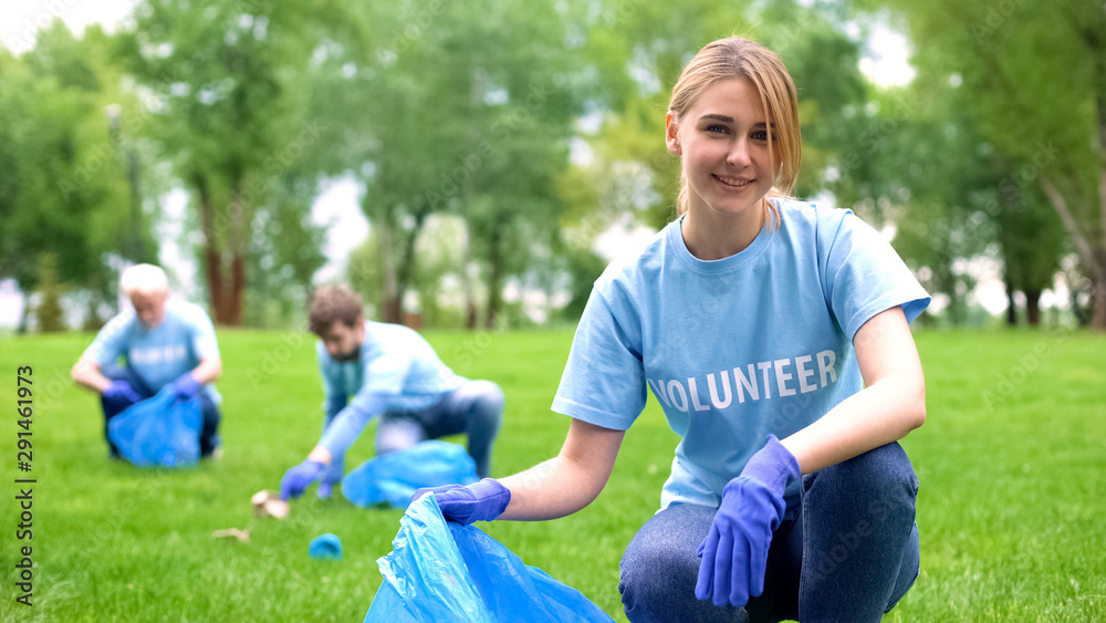 Pretty smiling female collecting forest garbage, looking at camera, volunteering