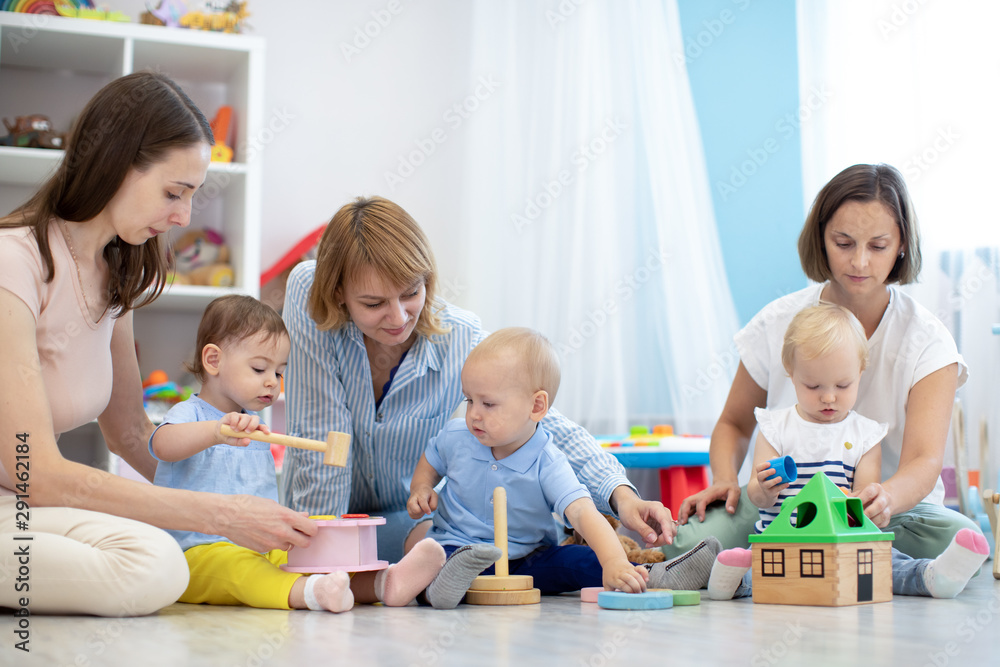 Group of workers with babies in nursery or kindergarten. Moms playing with kids in creche Group of workers with babies in nursery or kindergarten. Moms playing with kids in creche