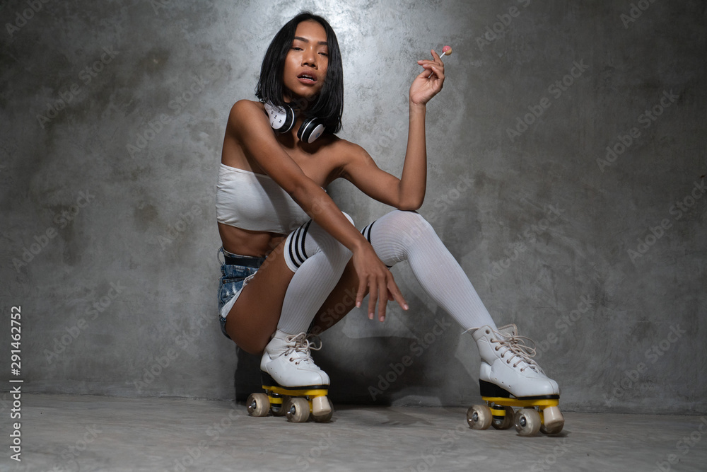 Young beautiful Asian girl in retro quads roller skates posing in studio over concrete wall background