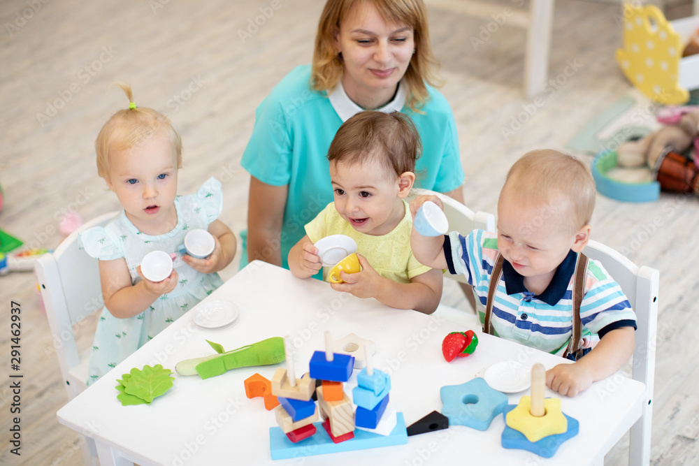 Worker with group of babies in creche. Top view of kids on lesson in kindergarten Worker with group of babies in creche. Top view of kids on lesson in kindergarten