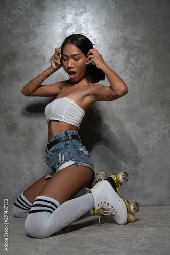 Young beautiful Asian girl in retro quads roller skates posing in studio over concrete wall background
