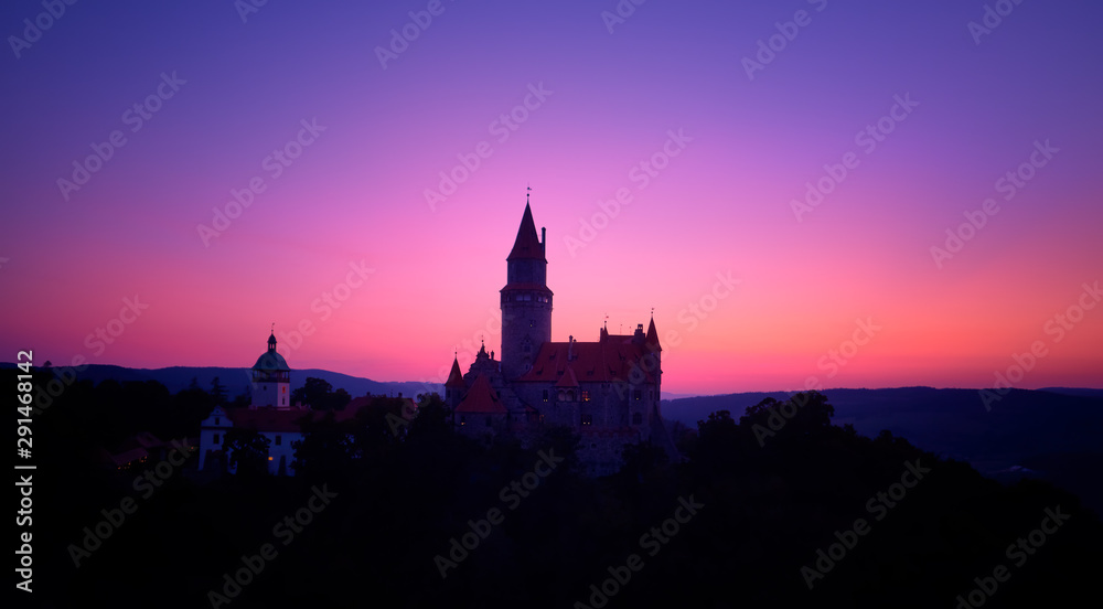 Aerial view on a silhouette of romantic fairytale castle in picturesque highland landscape, against pink and violet evening sky. Castle Bouzov with many towers, Moravia landscape, Czech republic.