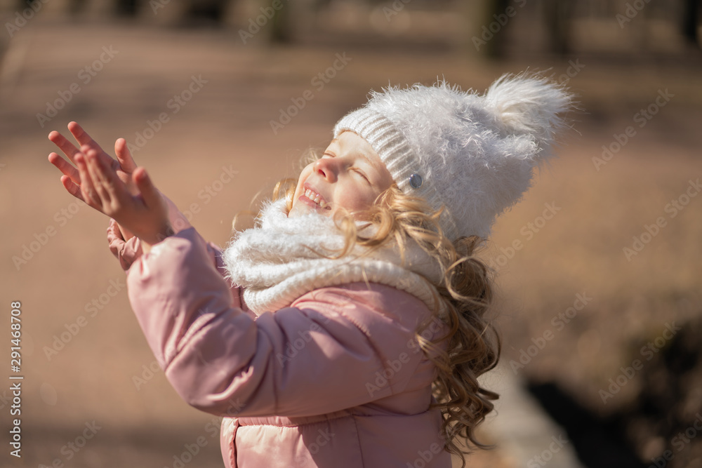 Pretty little girl in pink jacket catch the sunlight and walking in the cold spring city park alone Pretty little girl in pink jacket catch the sunlight and walking in the cold spring city park alone