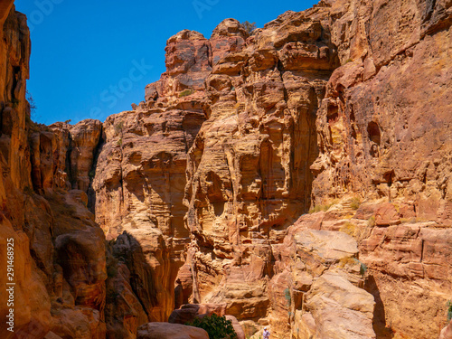 Steep cliffs of a canyon leading to the historical site of Petra  Jordan  light shining from blue sky on dark sandstone walls