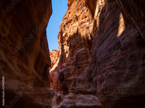 Steep cliffs of a canyon leading to the historical site of Petra  Jordan  light shining from blue sky on dark sandstone walls