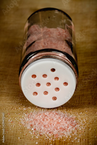 Glass salt shaker with pink Himalayan salt on a wooden chopping board