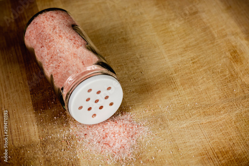 Glass salt shaker with pink Himalayan salt on a wooden chopping board