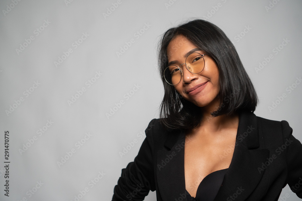 Portrait of attractive young Asian smiling woman in elegant black blazer and glasses posing over light gray wall background. Mock up copy space Portrait of attractive young Asian smiling woman in elegant black blazer and glasses posing over light gray wall background. Mock up copy space