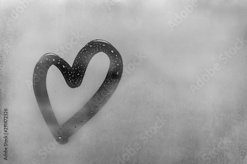 Heart painted on sweaty glass, there are many drops on it, inscription heart and love using handmade on wet gray autumn foggy glass