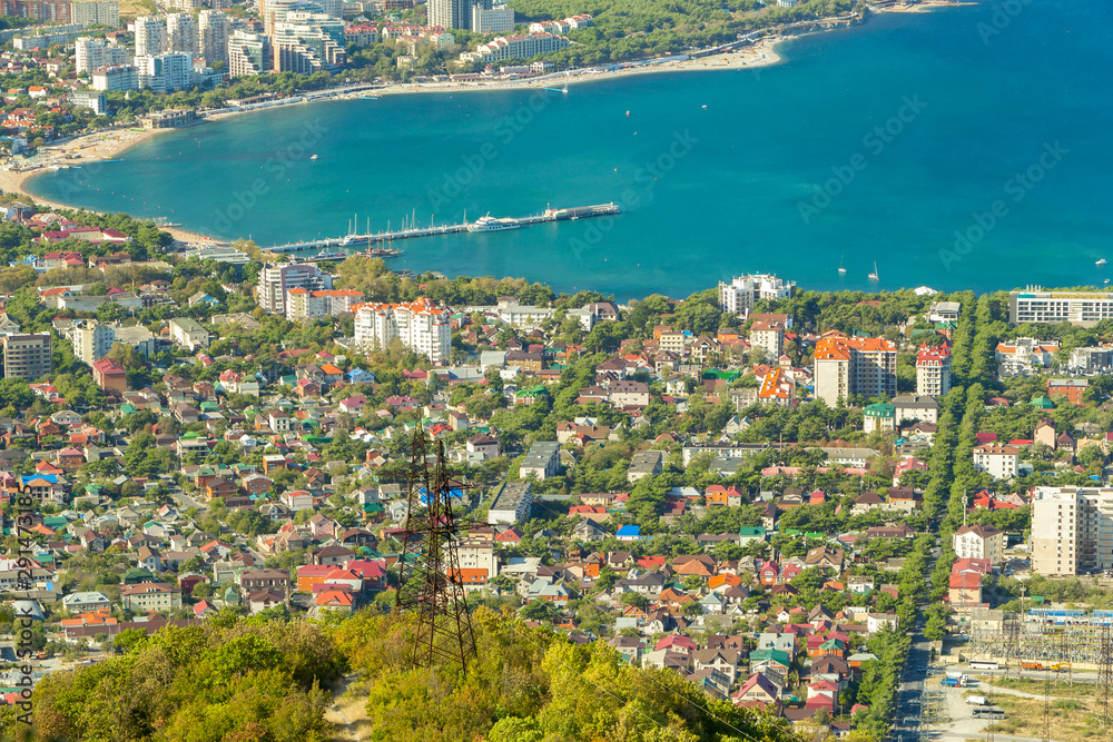 Aerial view of Gelendzhik resort city district from hill of caucasian mountains. Buildings, beaches and blue water of sea bay in frame.