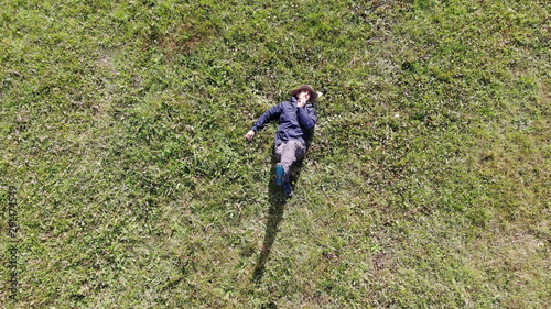 Bird eye view shot of a caucasian or Hispanic man laying down on green grass on a sunny day. relaxing CONCEPT aerial shot