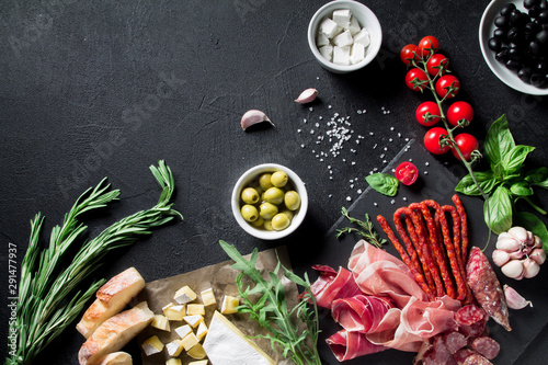A variety of meat and cheese snacks, sliced jamon and prosciutto, anchovies, olives, feta cheese and brie on a black background. Top view with copy space for your text