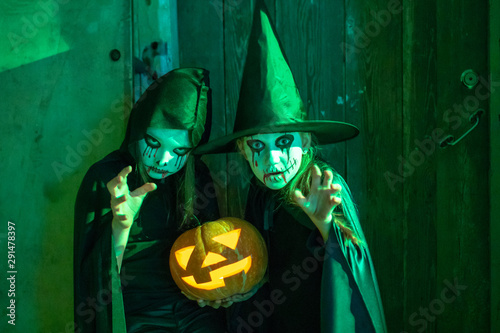 Two little teenage girls in zombie costumes hold a pumpkin in their hands in an old building and look frighteningly at the camera. Halloween and day of the dead concept. Toned. photo