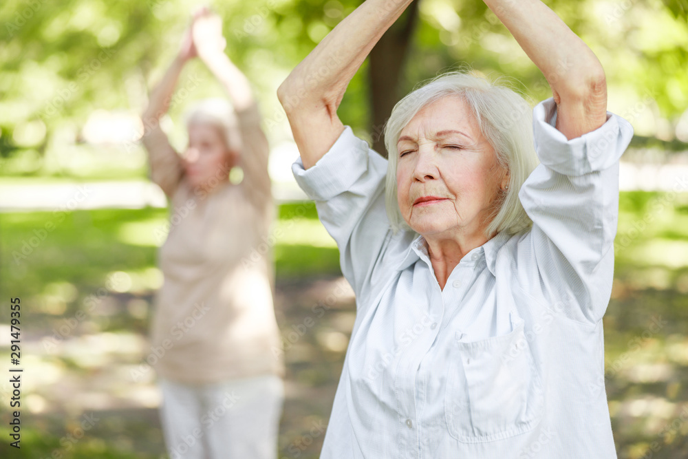 Serene old woman doing qigong exercise in the park Serene old woman doing qigong exercise in the park