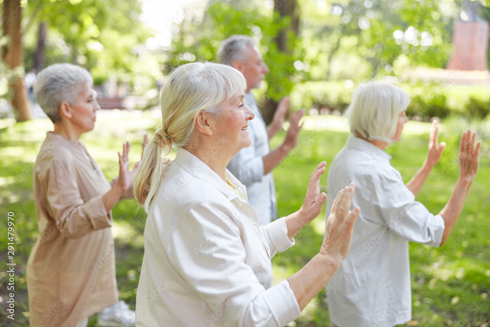 Fototapeta premium Smiling old lady practicing qigong with friends