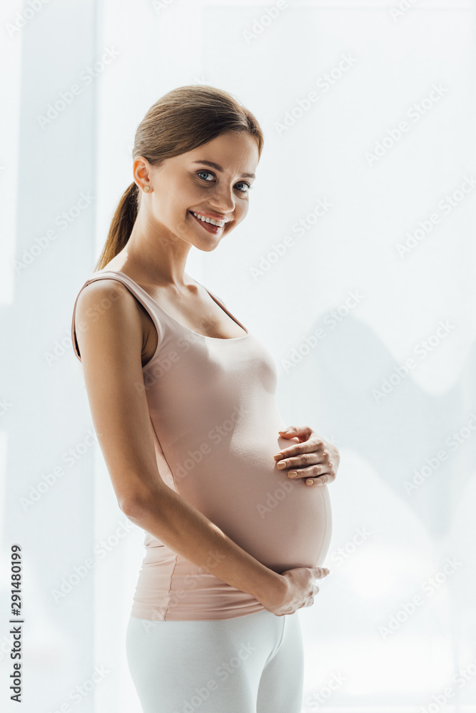 attractive pregnant young woman touching belly and looking at camera attractive pregnant young woman touching belly and looking at camera