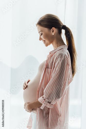 side view of happy pregnant woman smiling and touching belly