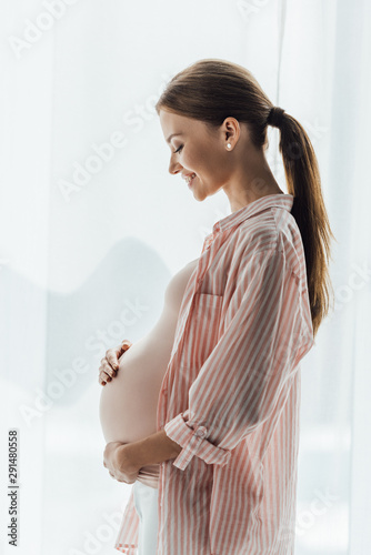 side view of happy pregnant woman smiling and touching belly