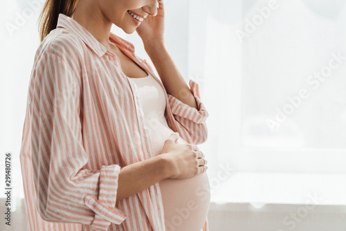 Fotografia partial view of happy pregnant woman smiling and touching belly