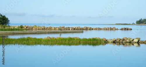 A small creek on the bay fenced with granite stones and grass. A clear summer morning. Blue water and clear sky.