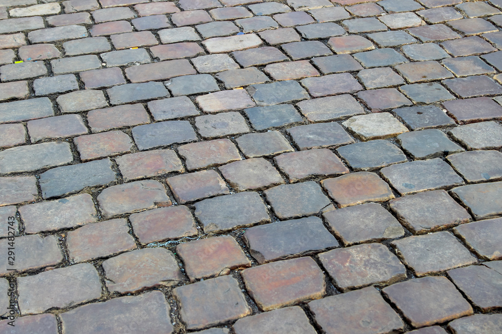 An old stoneblock pavement cobbled with rectangular natural stone blocks. Photo in perspective with selective focus