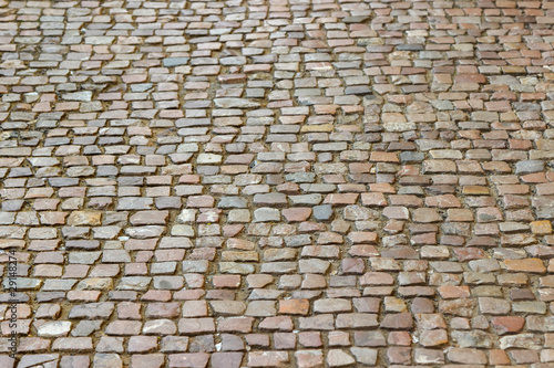 An old stoneblock pavement cobbled with natural stone blocks of different colors. Photo in perspective with selective focus