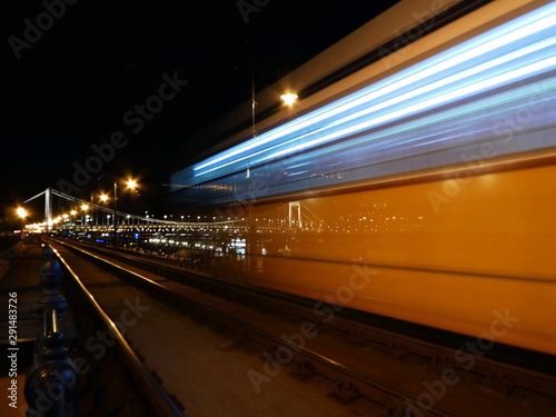 Yellow tramway passing by with reflection of Erzsebet bridge at night in Budapest, Hungary