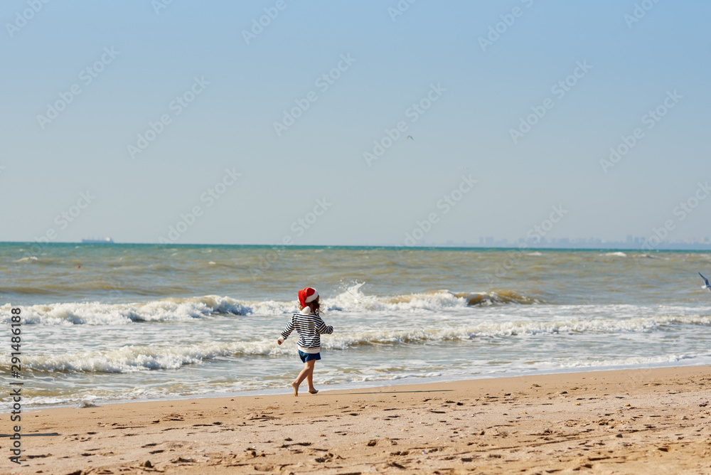 Little child girl in Santa red hat running and having fun on tropical beach. Christmas travel and vacation concept