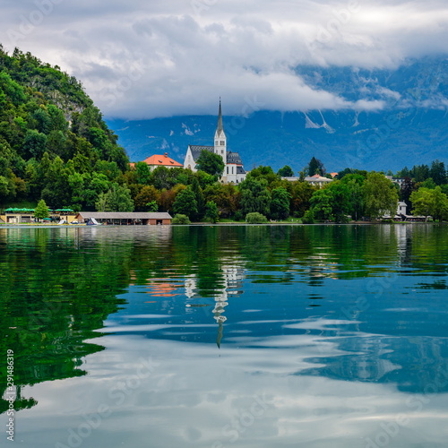 View of Lake Bled and St. Martin's Church with reflection. Clouds cover the tops of the mountains. © a_mikhail