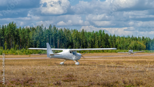 White single-engined ultralight airplane taxis for take off on a grassy airfield at sunny summer day.