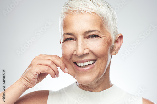 Gorgeous smiling Caucasian senior woman with short gray hair pinching her cheek. Beauty photography. photo