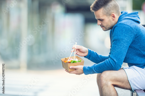 Young man having lunch asian food from box of recycled paper