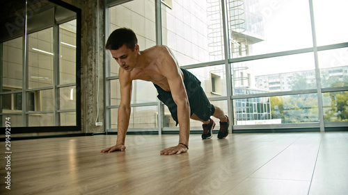 An athletic half naked man doing push-ups in the studio