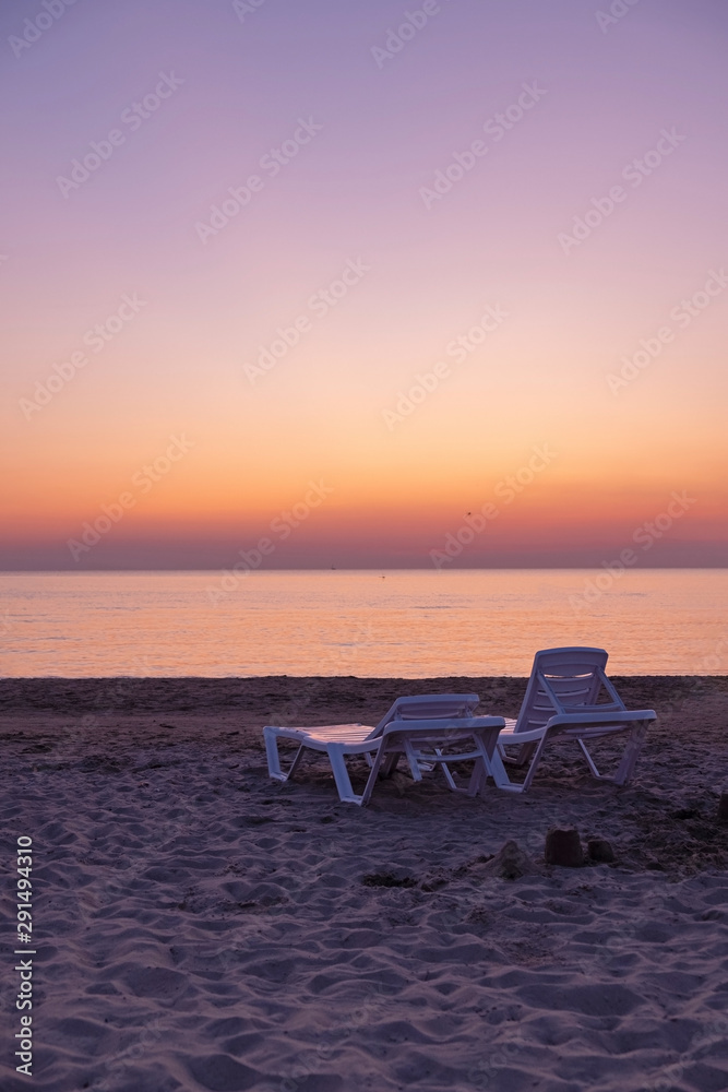 Sun loungers are on the sand against the setting sun. Sun loungers are on the sand against the setting sun.