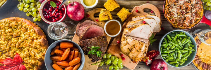 Thanksgiving family dinner setting concept. Traditional Thanksgiving day food  with turkey, green beans and mashed potatoes, stuffing, pumpkin, apple and pecan pies, rustic wooden table
