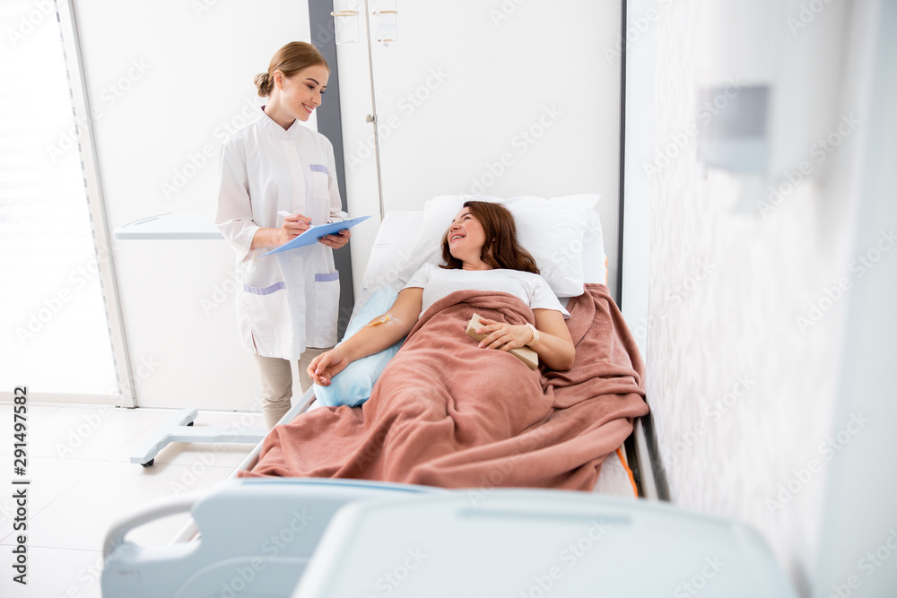 Female doctor looking at adult woman in bed Female doctor looking at adult woman in bed