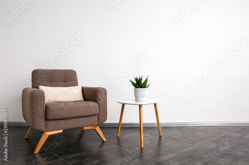 Comfortable armchair and table near light wall