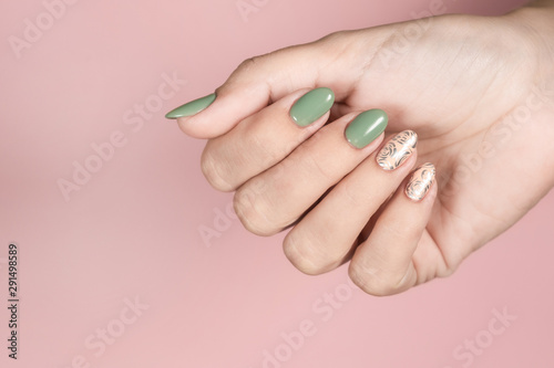 Closeup top view of beautiful trendy manicured fingernails painted in two colors: green and pink with silver stamping design. Female hand isolated on pink pastel background. Horizontal color photo.