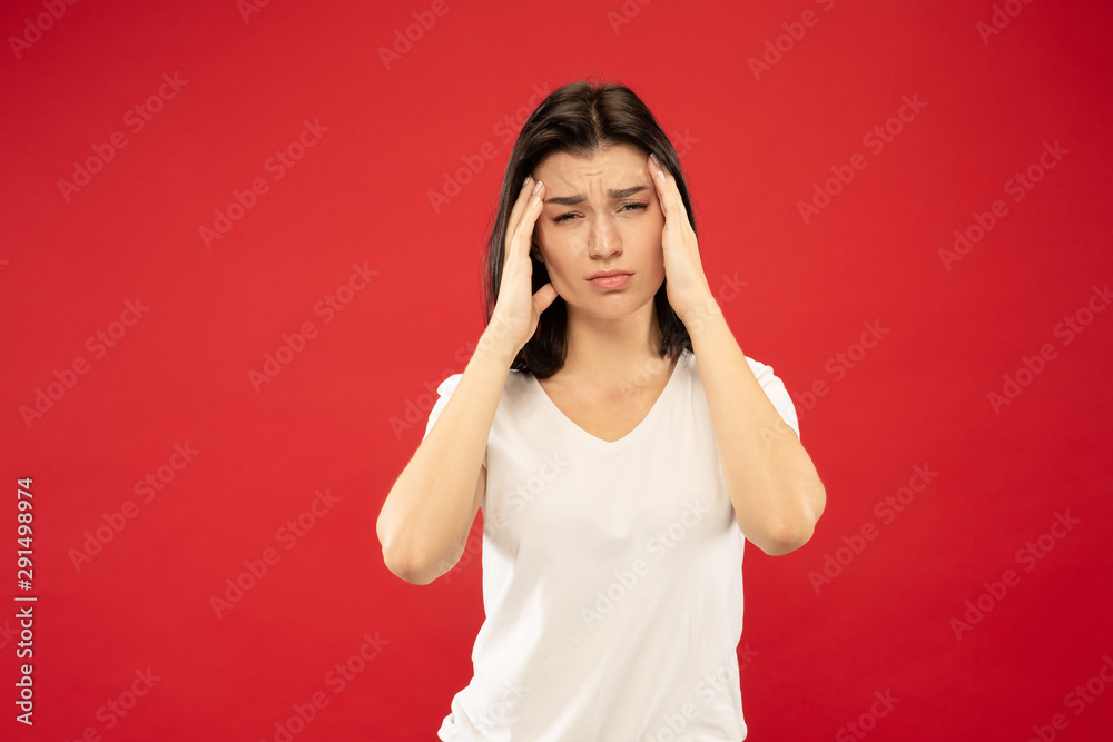 Caucasian young woman's half-length portrait on red studio background. Beautiful female model in white shirt. Concept of human emotions, facial expression. Suffering from headache, feeling ill. Caucasian young woman's half-length portrait on red studio background. Beautiful female model in white shirt. Concept of human emotions, facial expression. Suffering from headache, feeling ill.