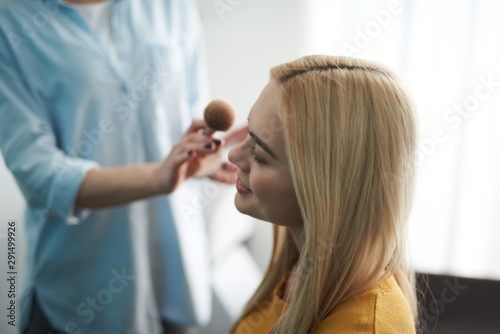 Talented makeup artist applying powder on lady face