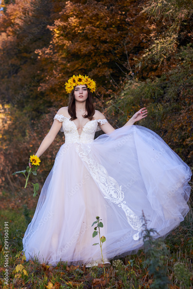 Beautiful cute sexy girl in a white dress with a wreath of sunflowers on her head enjoying nature. Autumn time.