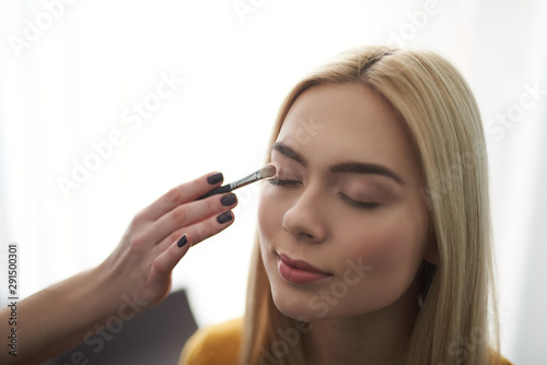 Skilful makeup artist applying beige eyes shadows on lady eyelids