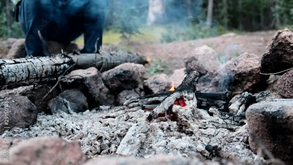 Camper sitting by the nearly extinguished fire pit. Static. Low POV. Soft focus Camper sitting by the nearly extinguished fire pit. Static. Low POV. Soft focus