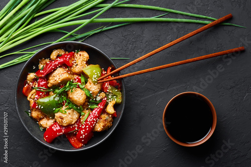 Schezwan Chicken or Dragon Chicken in black bowl at dark slate background. Szechuan Chicken is popular indo-chinese spicy dish with chilli peppers, chicken and vegetables. photo