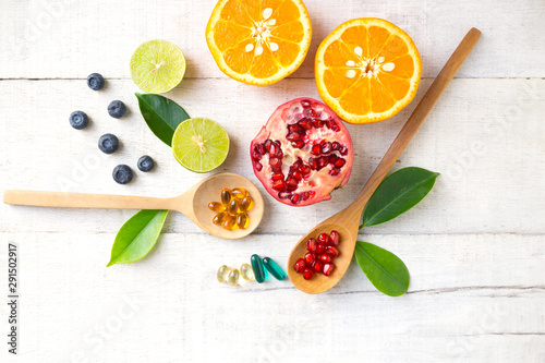 Multivitamin supplements on wooden spoon with healthy fruit blueberry, lime, orange, pomegranete on white wooden background. photo
