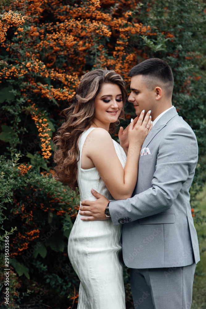 Fototapeta premium Beautiful wedding photos in summer. Beautiful young couple hugging among the branches of sea buckthorn. Beautiful couple are walking in the park at summer. Beautiful young couple tenderly kissing