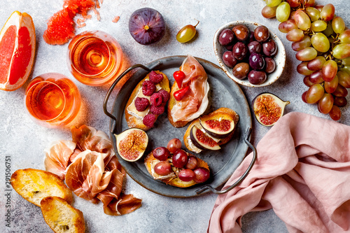 Appetizers, antipasti snacks and rose wine in glasses. Bruschetta or authentic traditional spanish tapas set, cheese and meat platter over grey concrete background. Top view