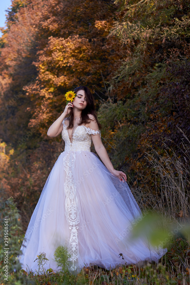 Beautiful cute young girl in a white dress with a flower of a sunflower. Enjoy nature Autumn time.