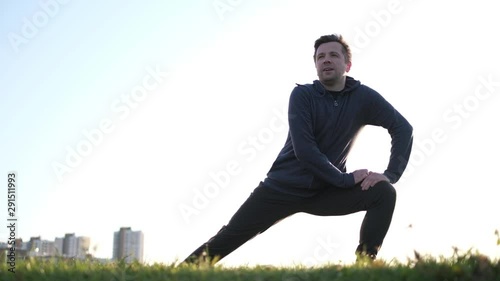 Young caucasian male athlete stretching legs in park for warming up.
