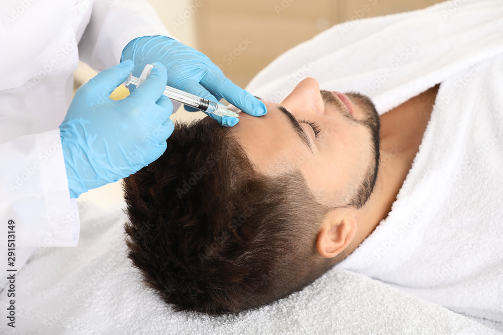 Handsome man receiving filler injection in beauty salon